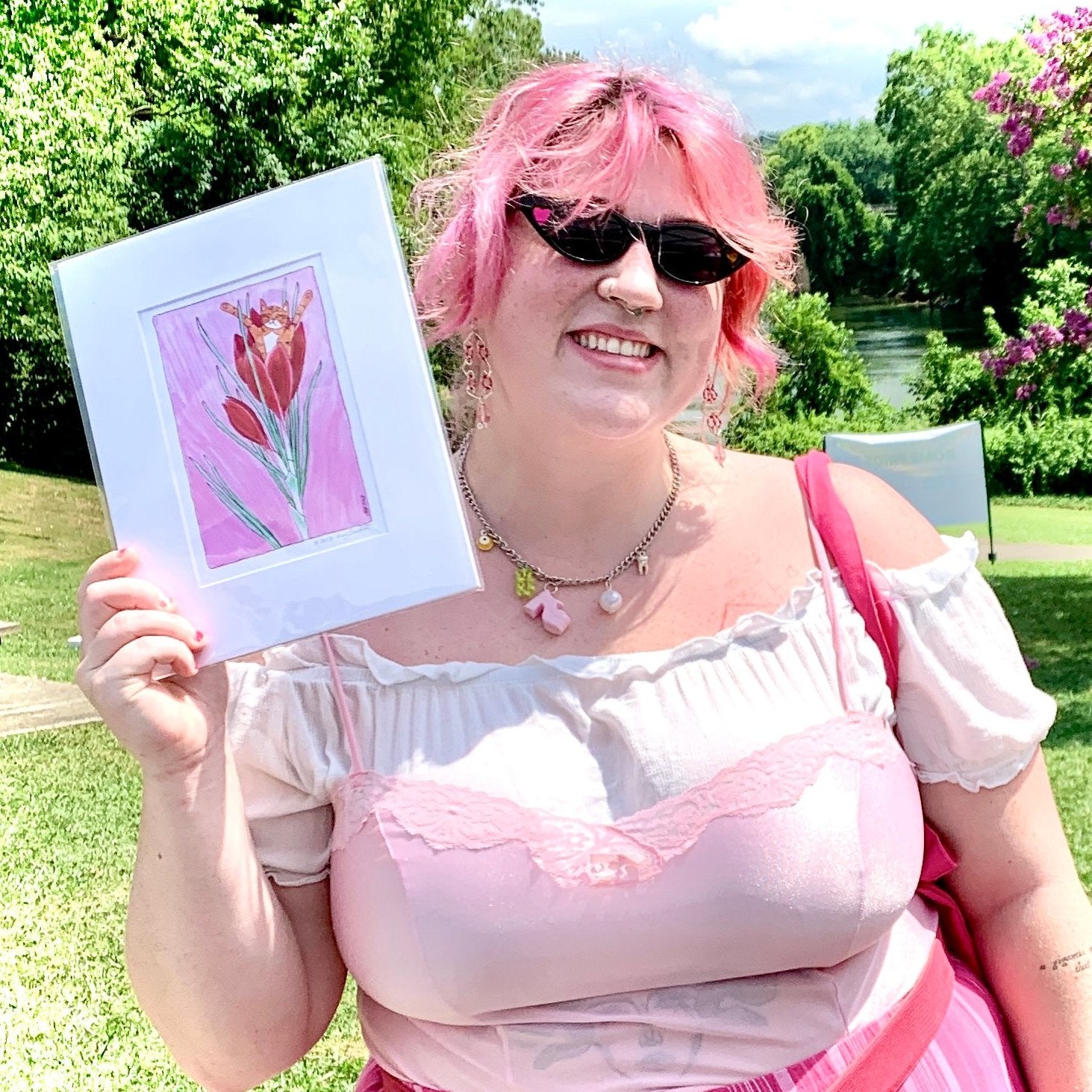 a woman in pink holding an art print of Superpussy, an orange cat sitting in a red flower on a pink background
